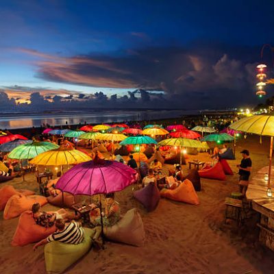 Seminyak, Indonesia - February 25, 2016: Seminyak beach at dusk. People chilling out, having drinks, laying on puffs, under colourful lit parasols